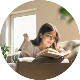 A woman sits comfortably reading a book, bathed in soft sunlight, in a cozy, indoor setting.